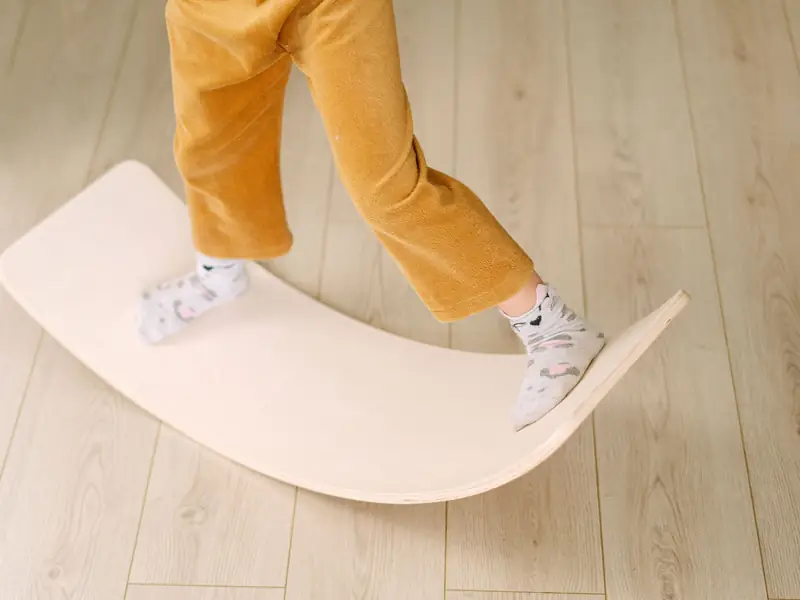 Kinderbeine in Socken balancieren auf einem gebogenen Balancierbrett aus Holz.