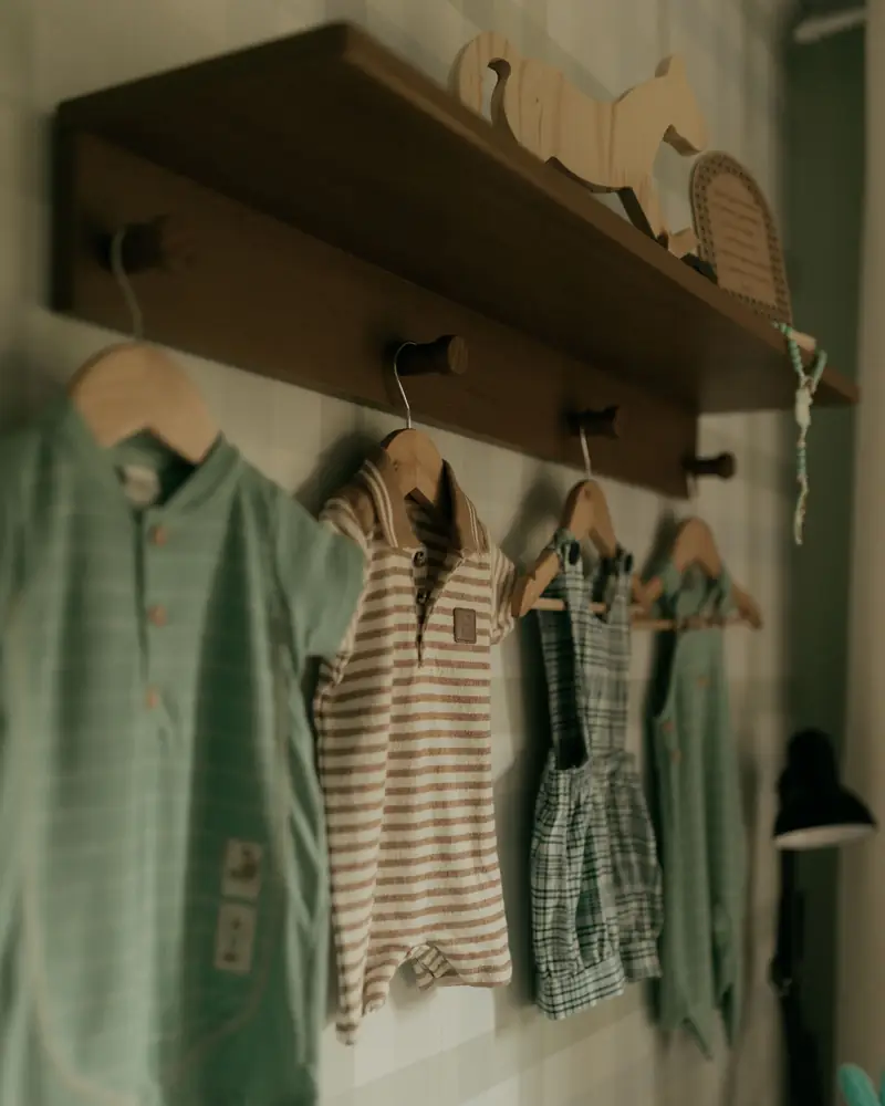 Kleine Kinderkleidung hängt auf Holzbügeln an einer Garderobenleiste.